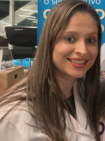 Débora de jaleco branco sorrindo diante do banner dela numa academia