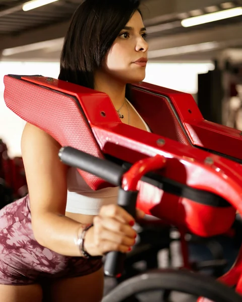 Mulher concentrada treinando num aparelho vermelho da academia