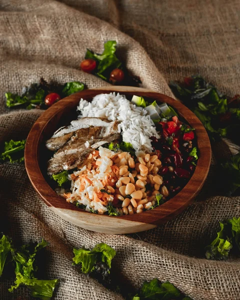 Tigela rústica com frango grelhado, arroz e grão-de-bico sobre folhas verdes