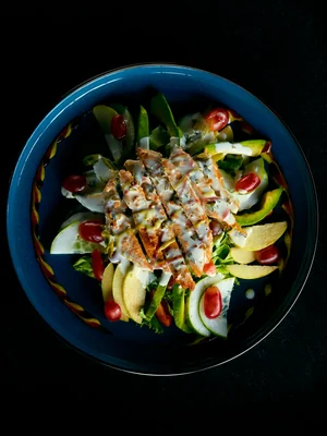 Tigela azul com frango, abacate, folhas e legumes